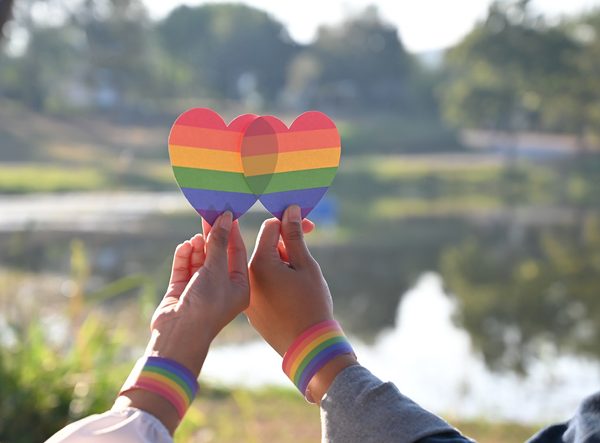 Closeup of LGBT couple while they are holding a rainbow hearts on hand. LGBT happiness concept.